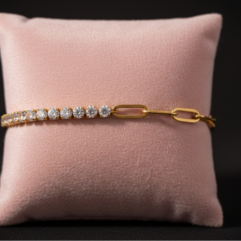 Primer plano de una pulsera estilo mitad tennis y mitad eslabones paperclip dorados, sobre un cojín de terciopelo rosa pálido. Pulsera dualidad de acero inoxidable, con baño de oro 18k y circonitas. Joyería de moda elegante y resistente al agua.