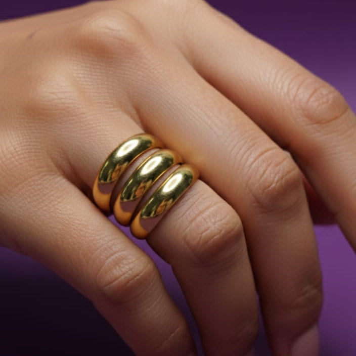 anillo ancho dorado con un diseño envolvente de tres bandas apiladas. Anillo de mujer estilo minimalista y statement en acero inoxidable con baño de oro 18k sobre fondo blanco. Joyería de moda de triple banda